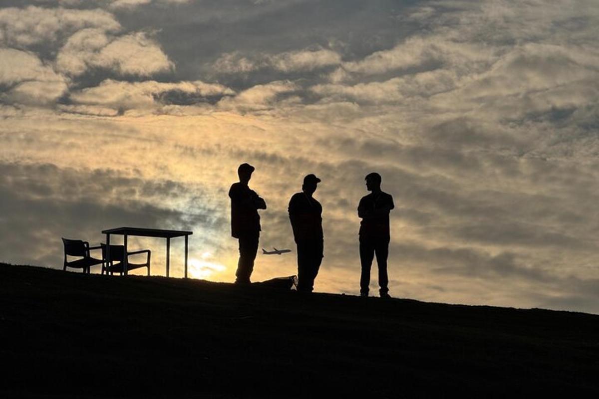 Tres hombres de pie en una colina mirando la puesta de sol