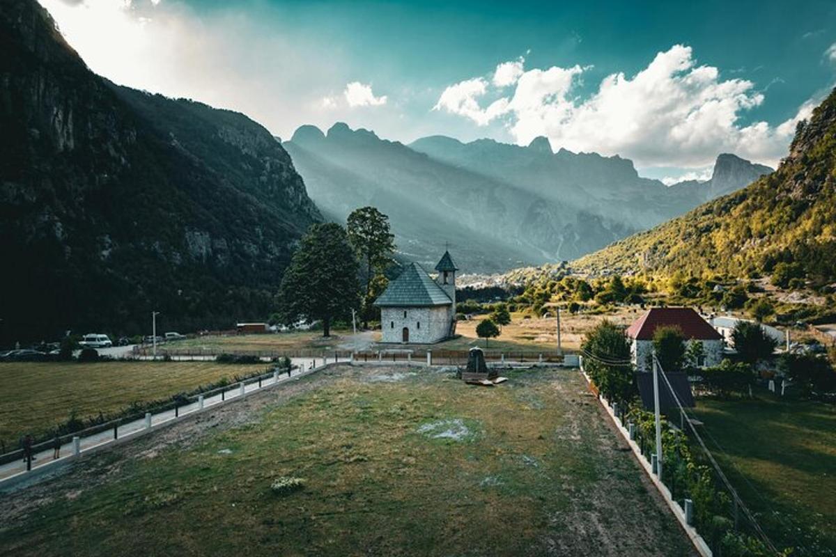 a small church in a field with mountains in the background