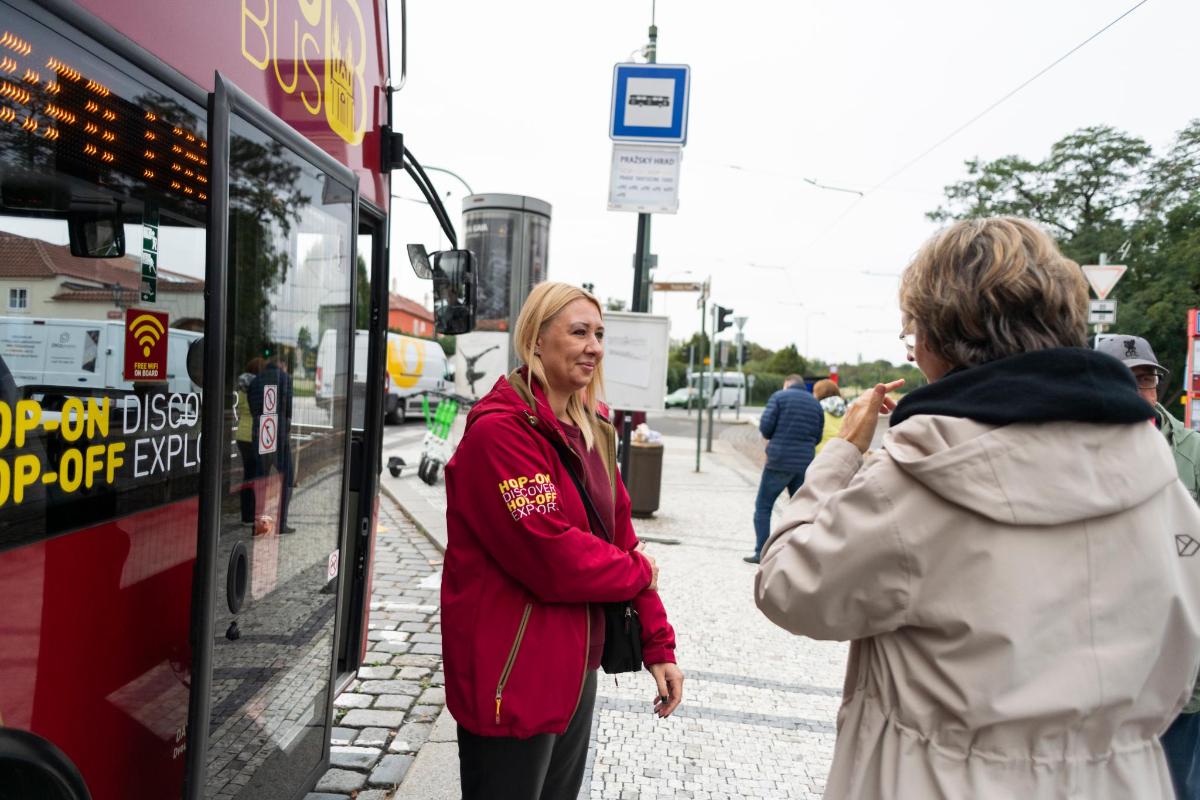 kona stendur á gangstétt við hliðina á strætó