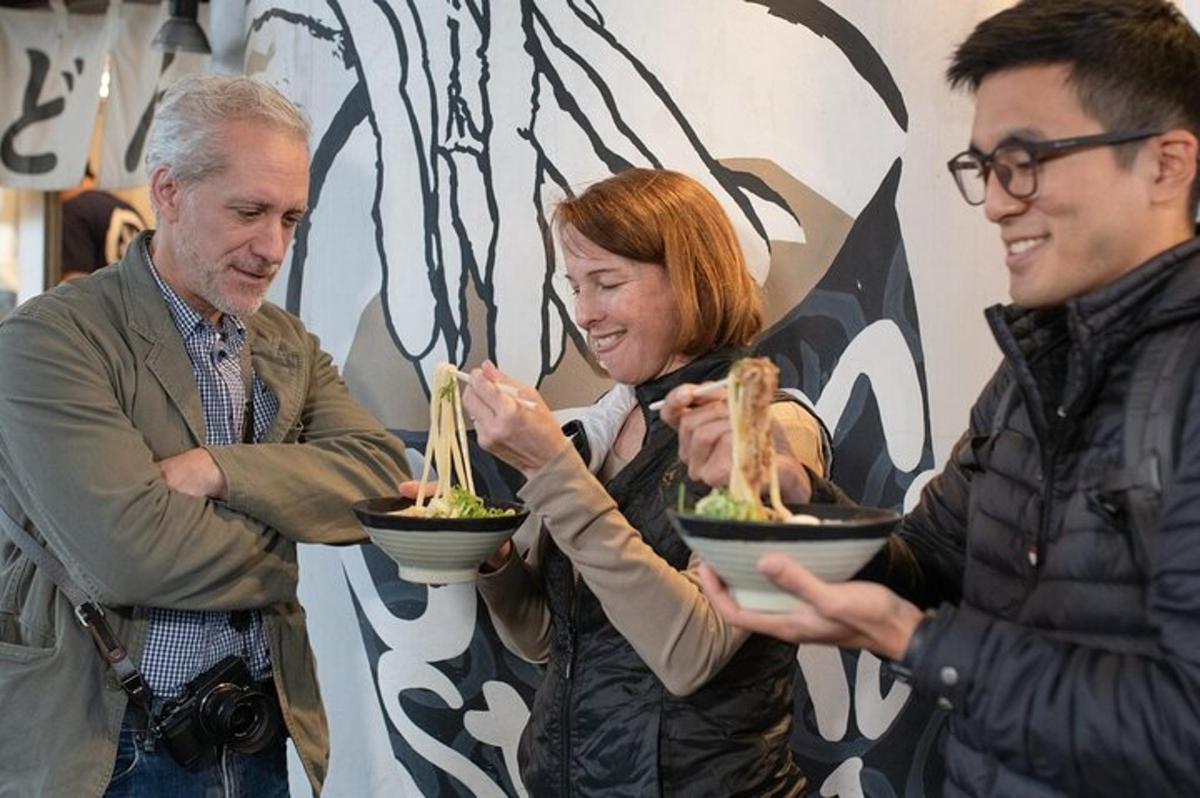 a woman holding noodles in a bowl with two men