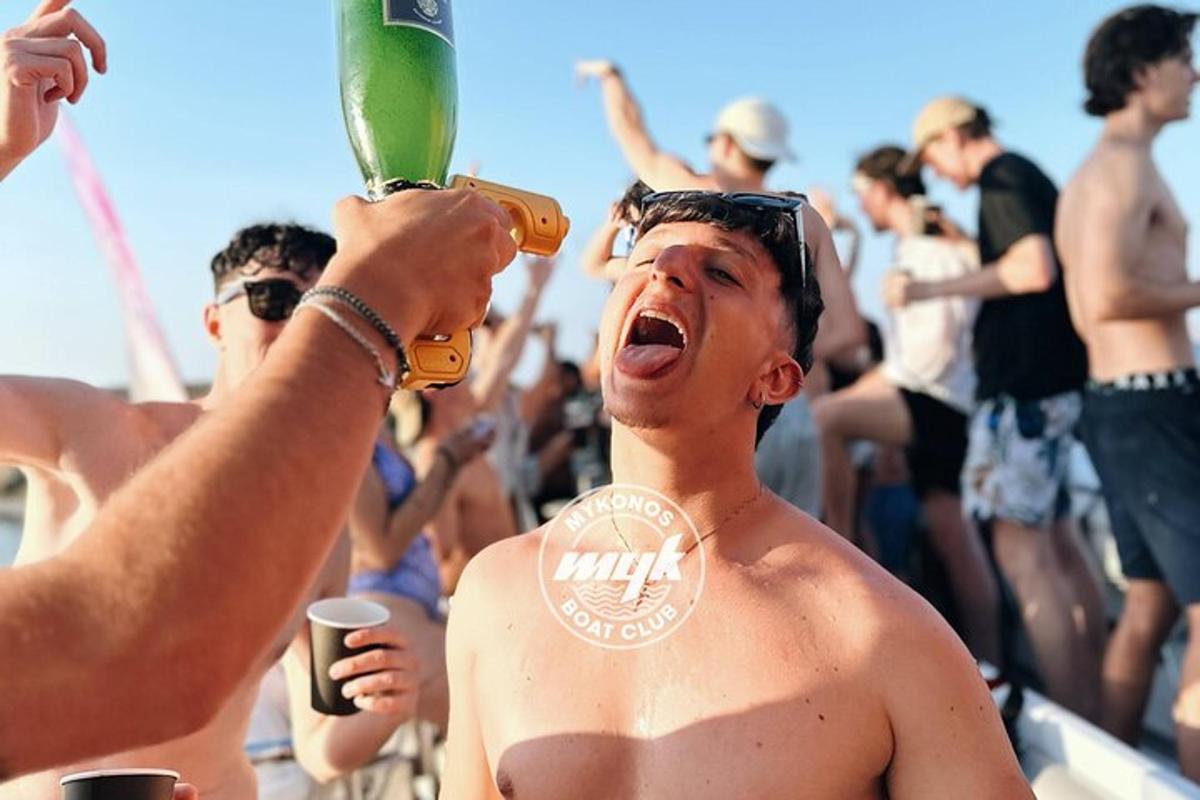 Un hombre sin camisa bebiendo una bebida en una playa.