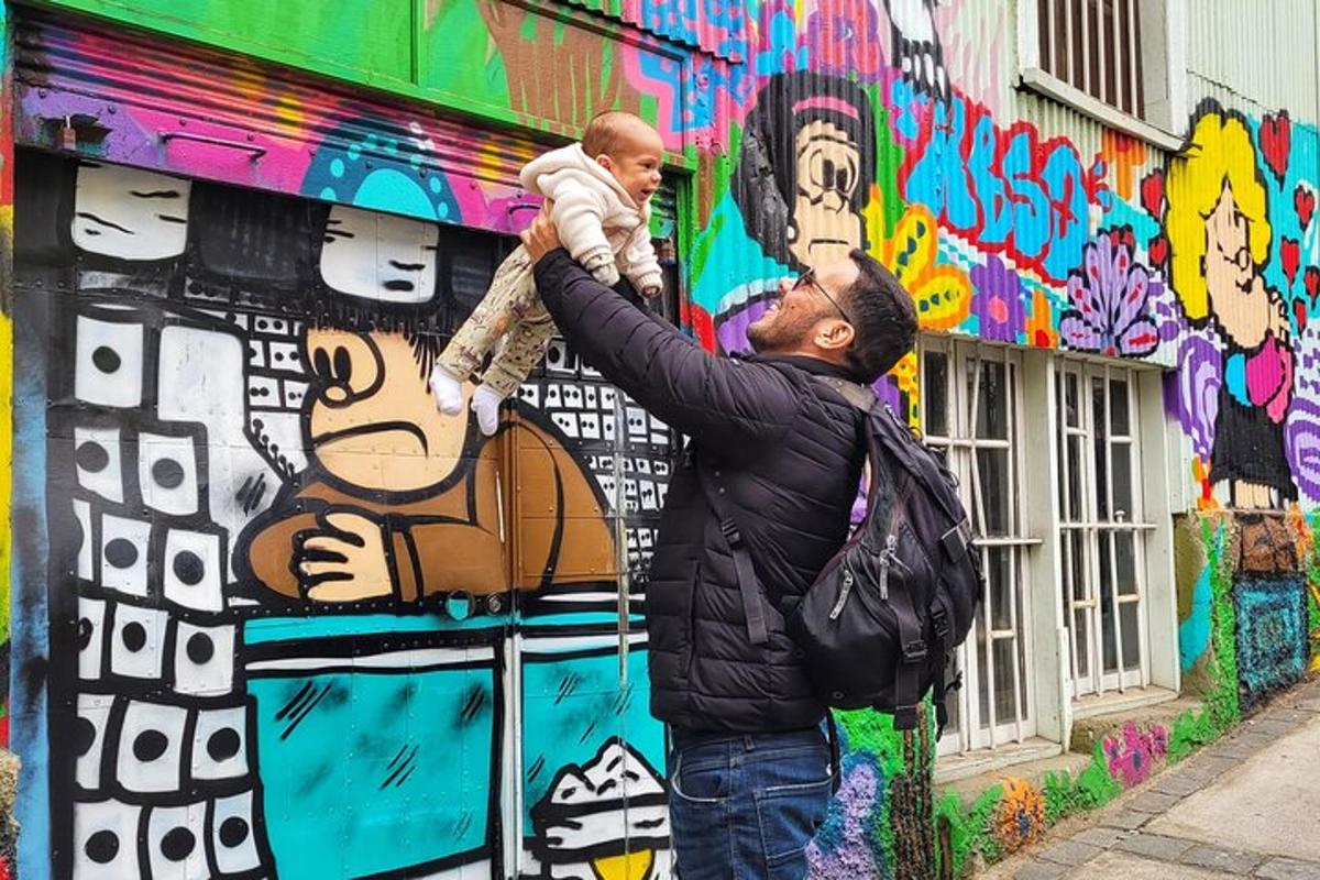 Un hombre sostiene a un bebé frente a una pared con grafitis.