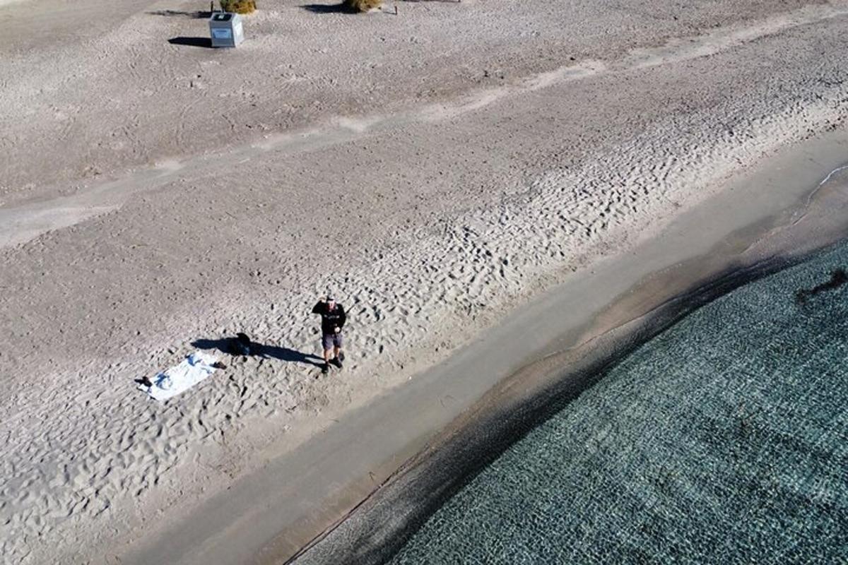 un home caminant per una platja vora l'aigua
