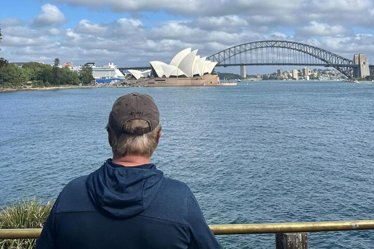 mies istuu kaiteella ja katsoo Sydneyn oopperataloa