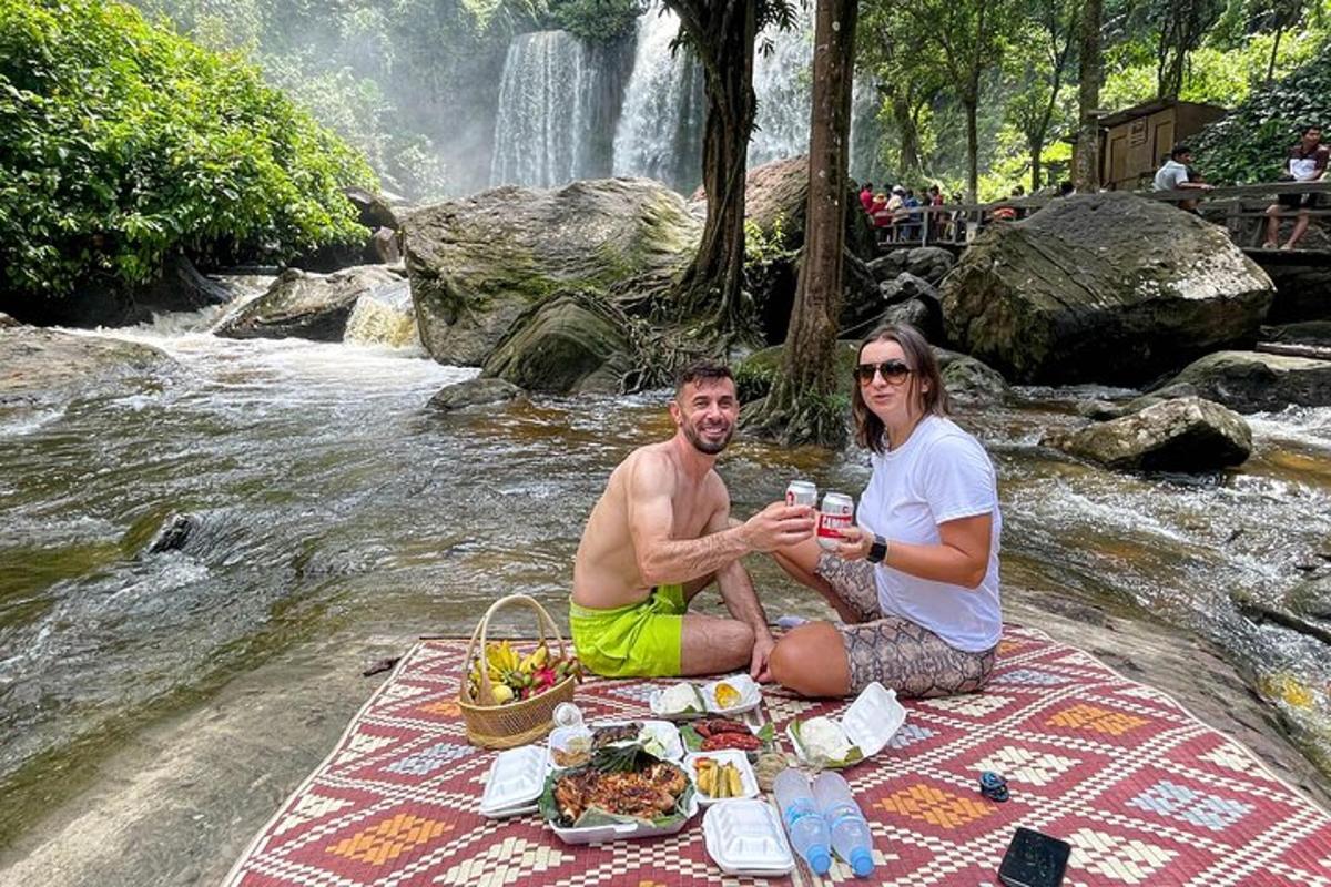 seorang lelaki dan wanita duduk di atas selimut berkelah di sebelah air terjun