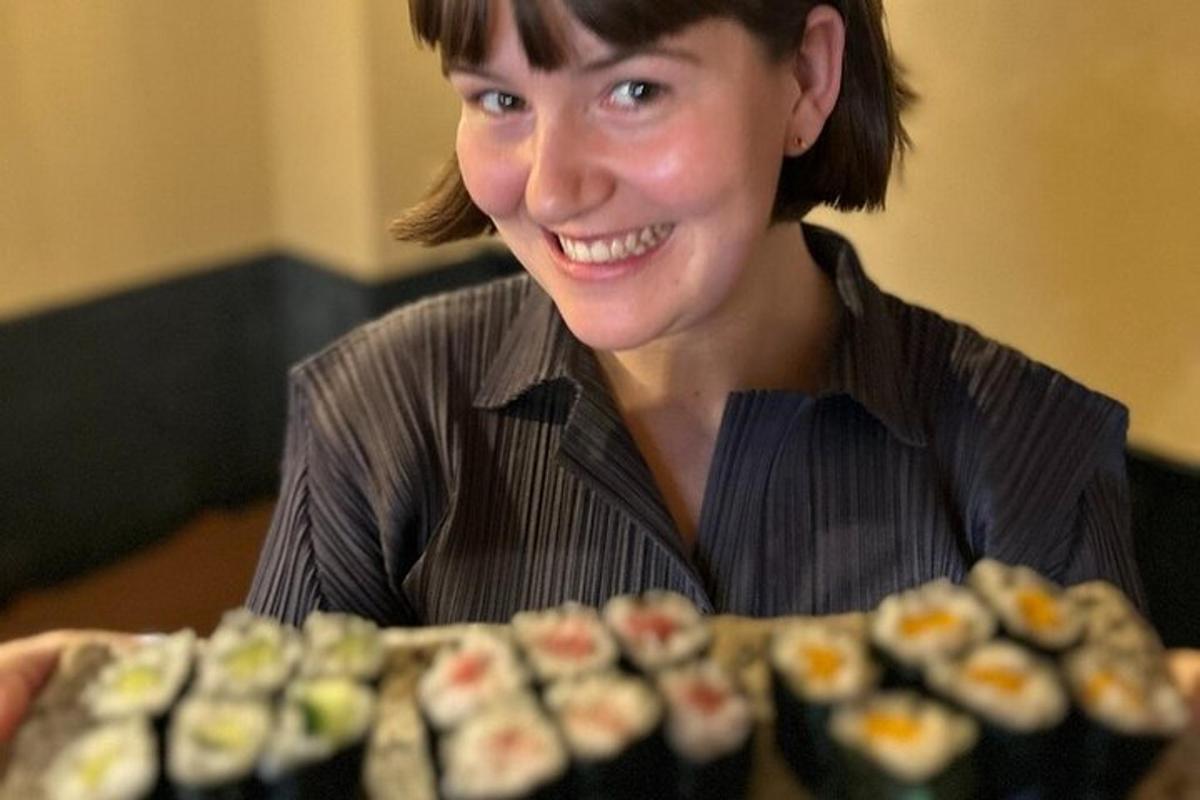 en kvinde smiler ved siden af en bakke sushi