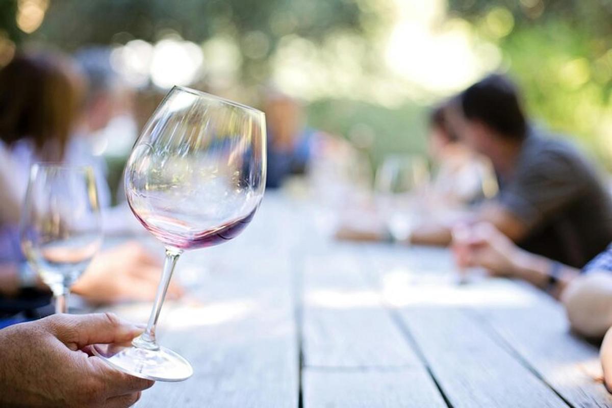 una persona che tiene in mano un bicchiere di vino su un tavolo di legno