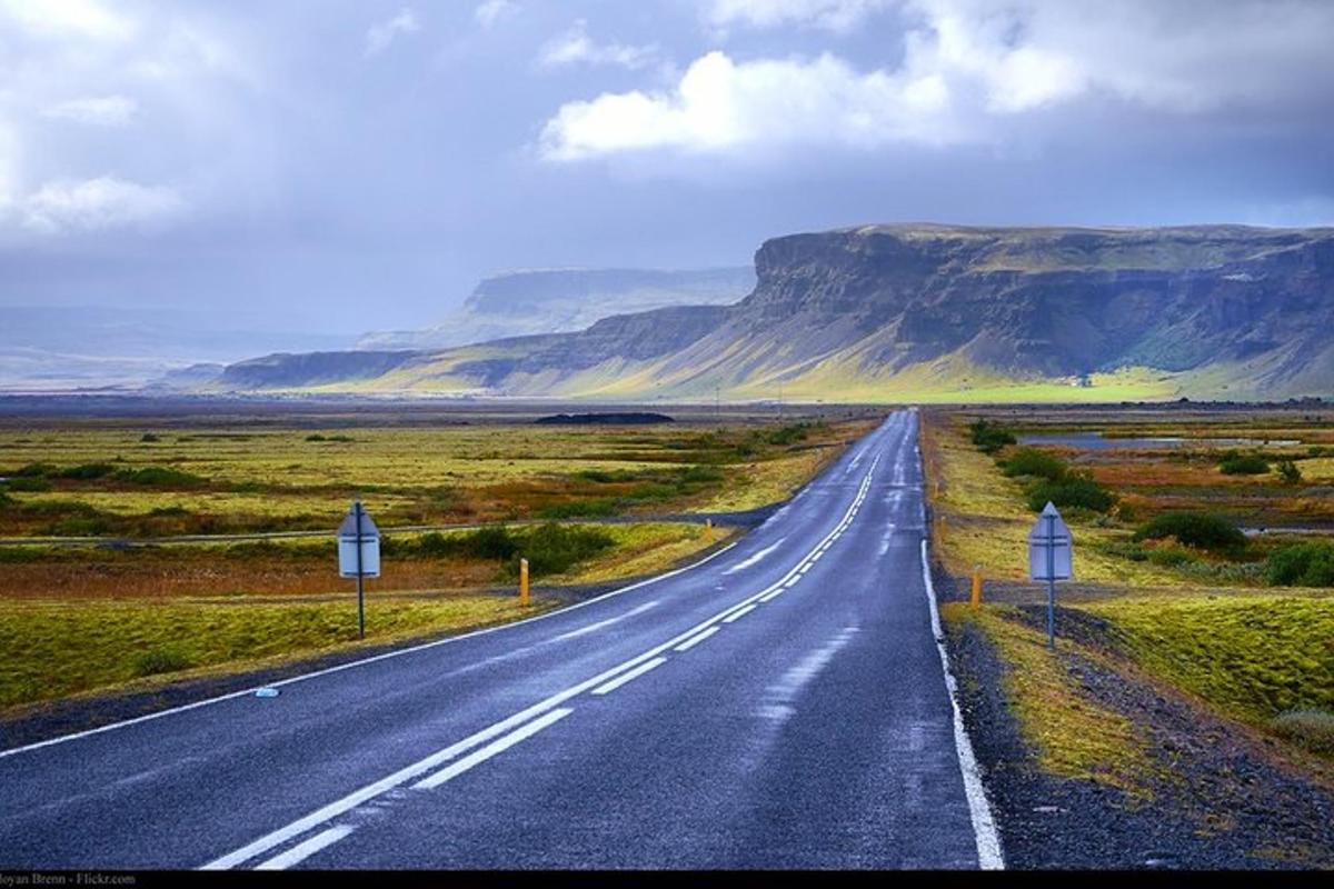 an empty road in the middle of a field with mountains