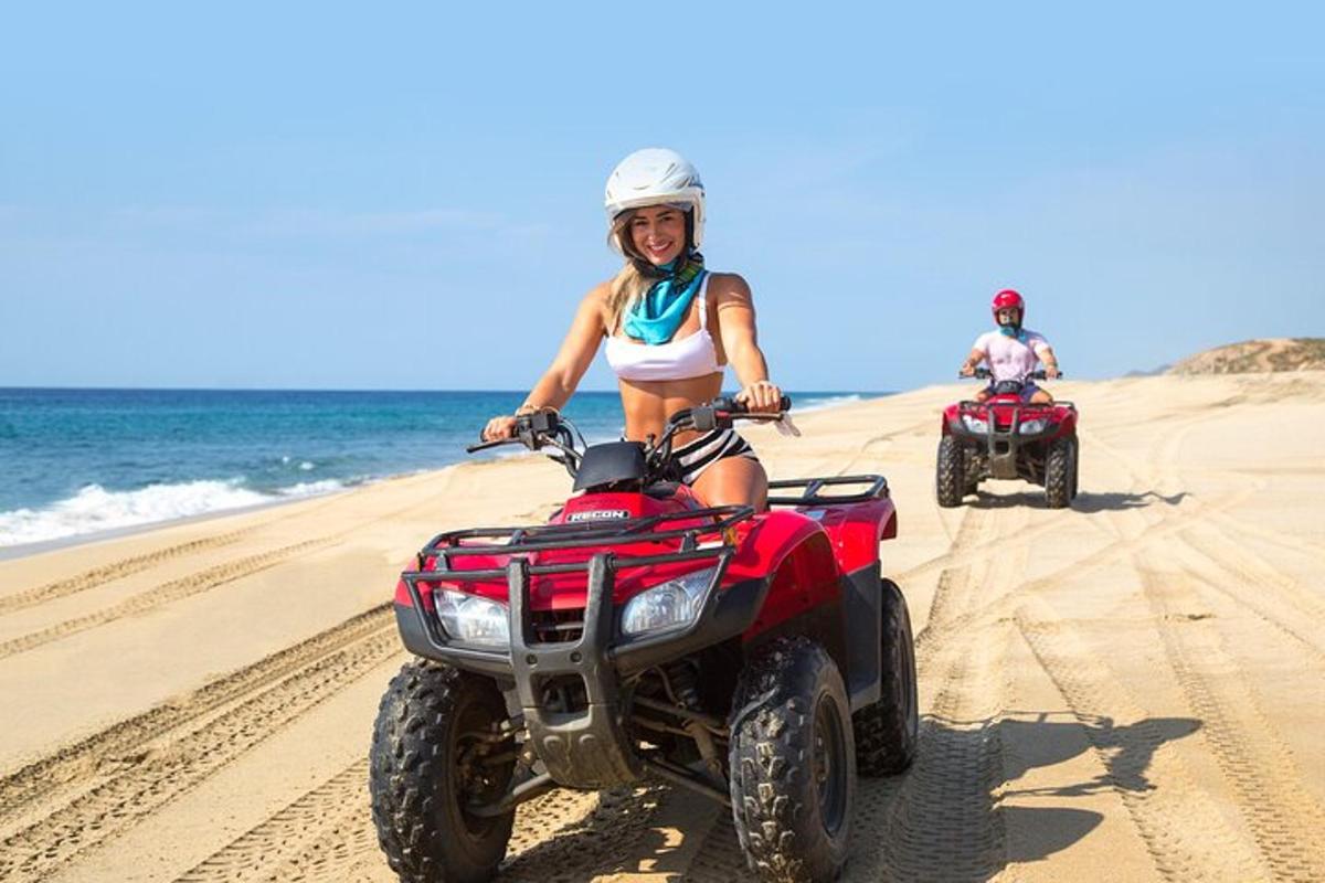 Două persoane merg cu ATV-uri pe plajă