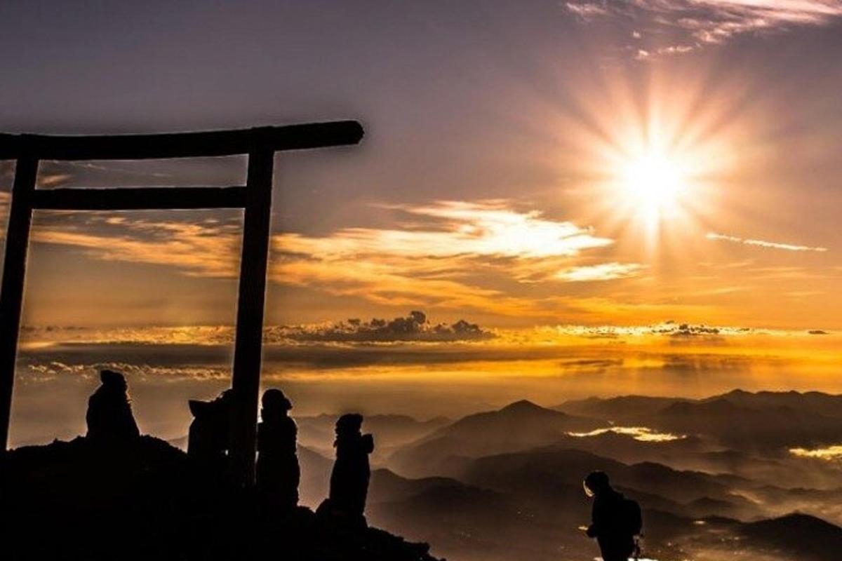 en gruppe mennesker som sitter på toppen av et fjell ved solnedgang