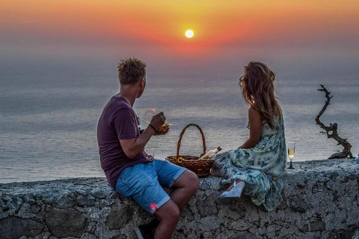 een man en een vrouw zitten op een muur en kijken naar de zonsondergang