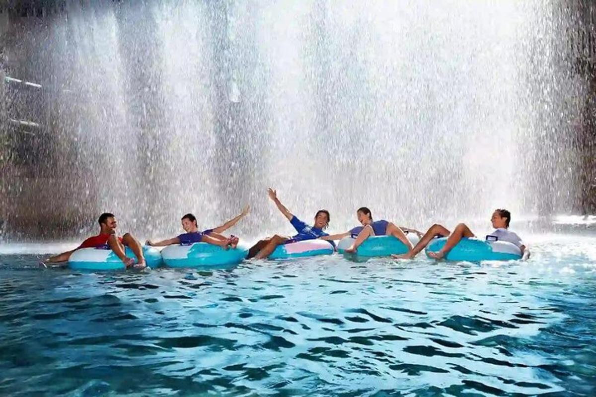 a group of people sitting in the water in front of a waterfall