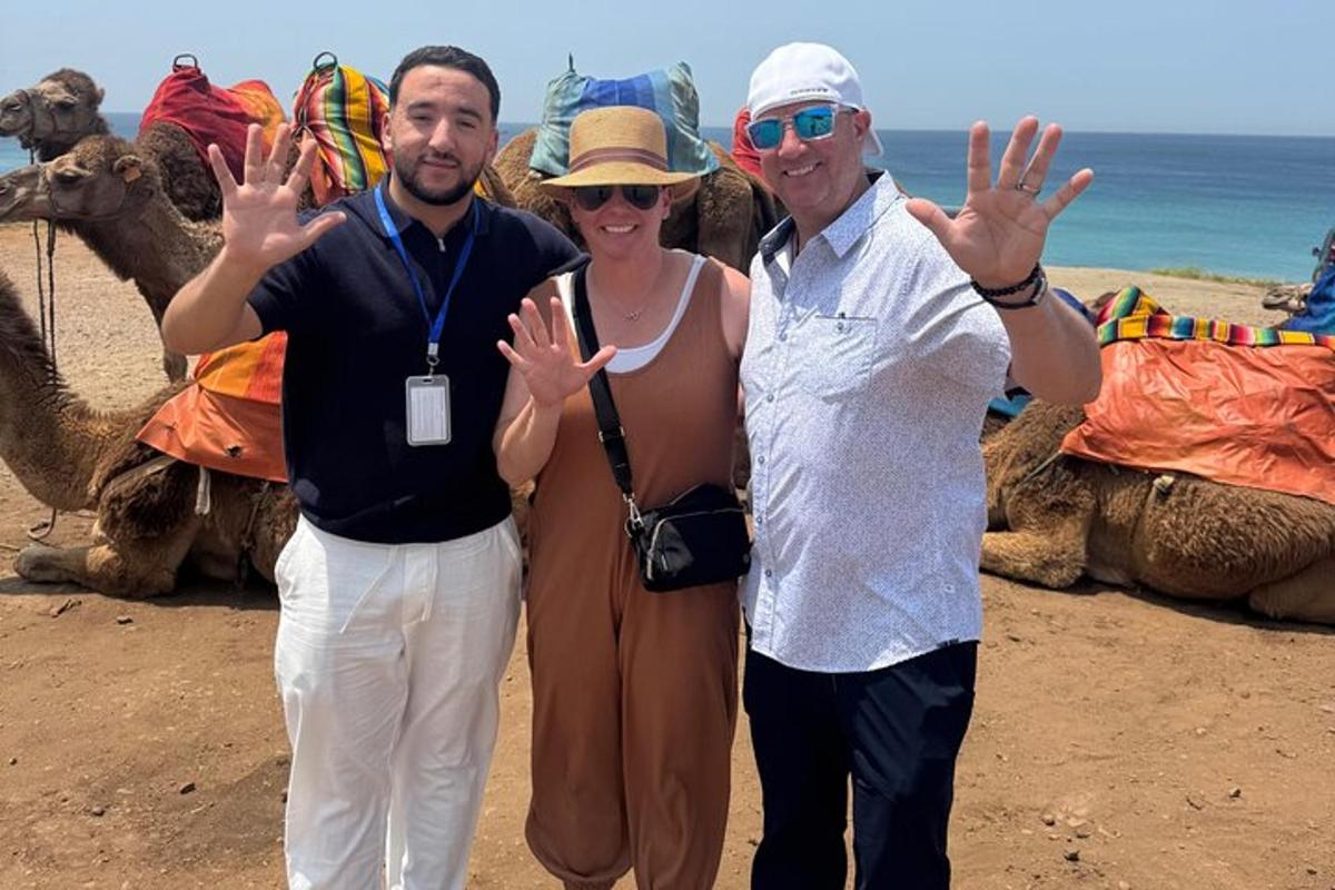 Dos hombres y una mujer de pie delante de camellos.