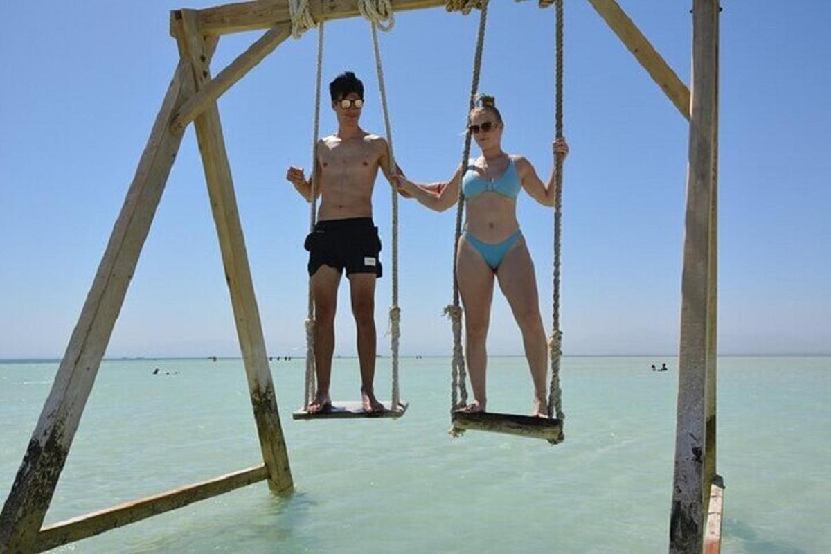 two people sitting on a swing on the beach