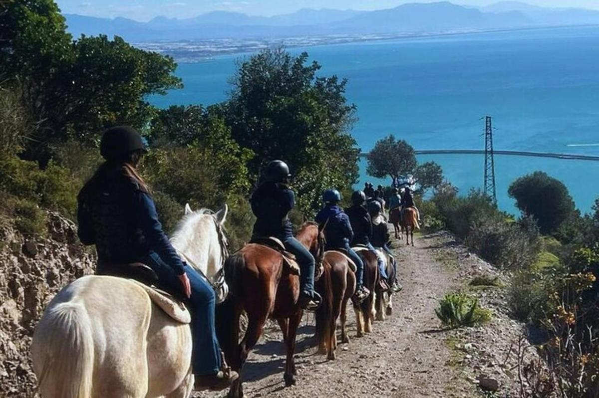 μια ομάδα ανθρώπων που καβαλούν άλογα κάτω από έναν λόφο