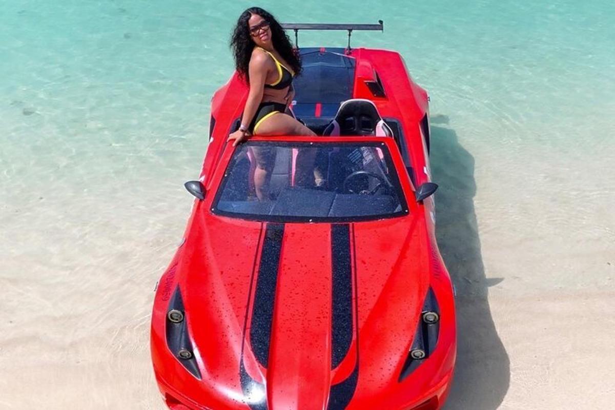 Una mujer sentada encima de un coche rojo en la playa.