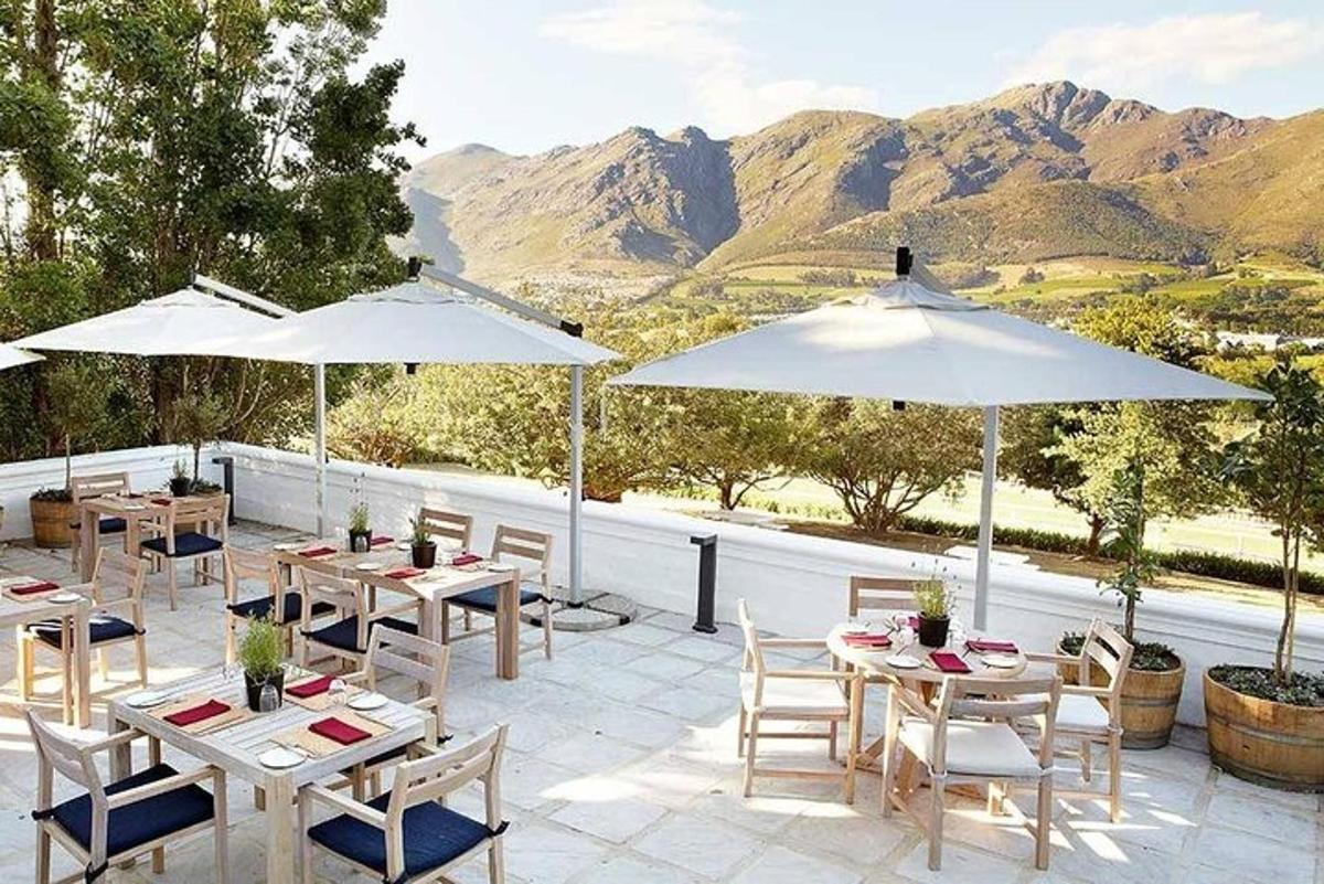 un patio con tavoli e ombrelloni con le montagne sullo sfondo