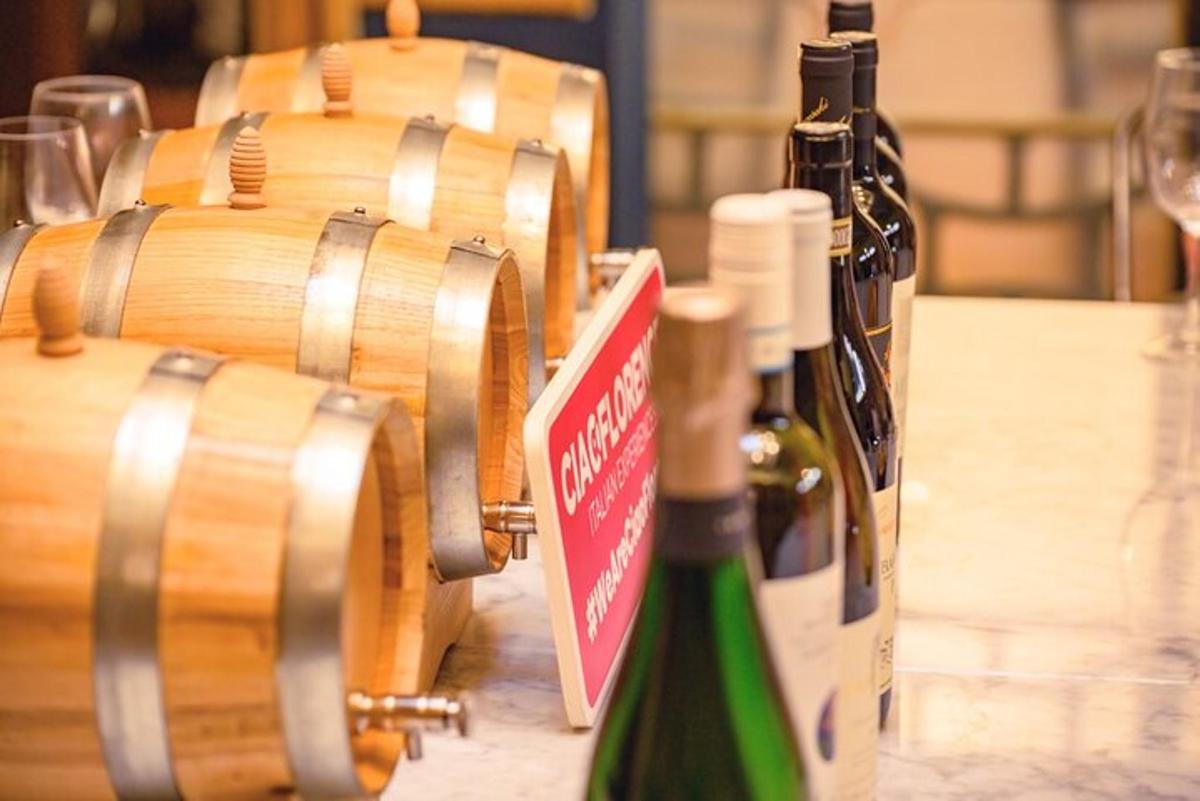 Δύο μπουκάλια κρασί κάθονται σε ένα τραπέζι δίπλα σε βαρέλια