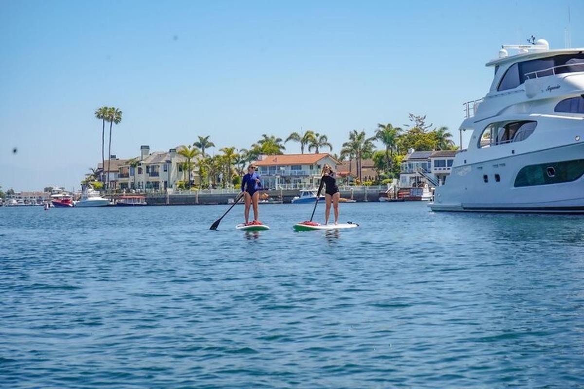 dva lidé na paddleboardech ve vodě s jachtou
