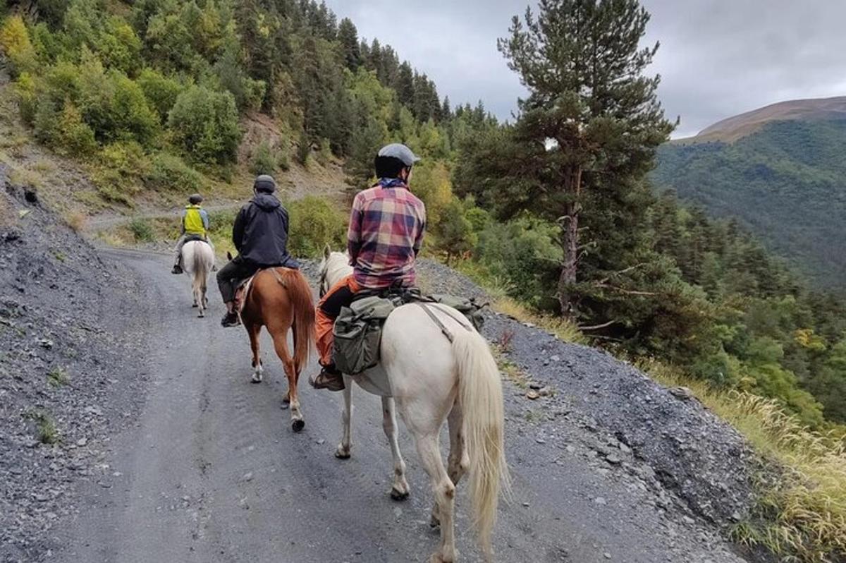 tre personer som rir på hester nedover en grusvei