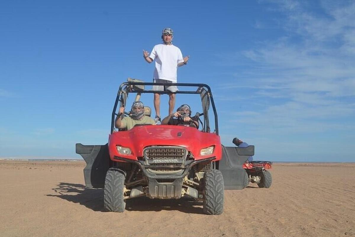Un hombre parado encima de un vehículo todoterreno rojo en el desierto.
