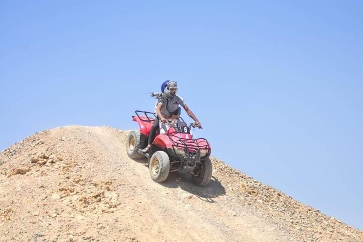 un home conduint un quad vermell per un camí de terra