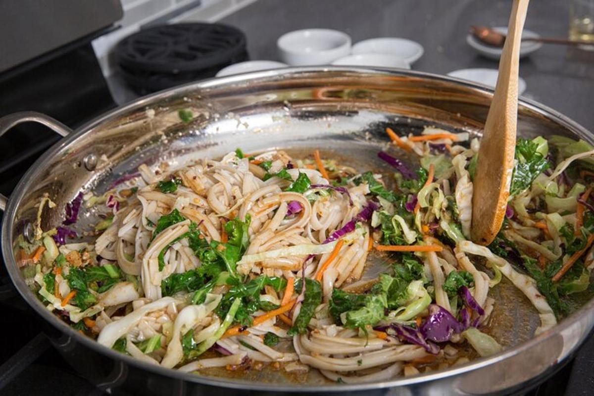 een wok gevuld met pastasalade met een houten lepel