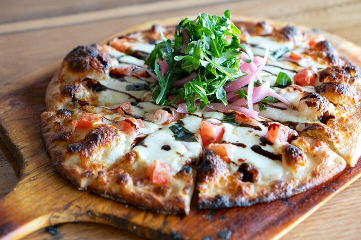 una pizza su un tagliere di legno con un'insalata sopra