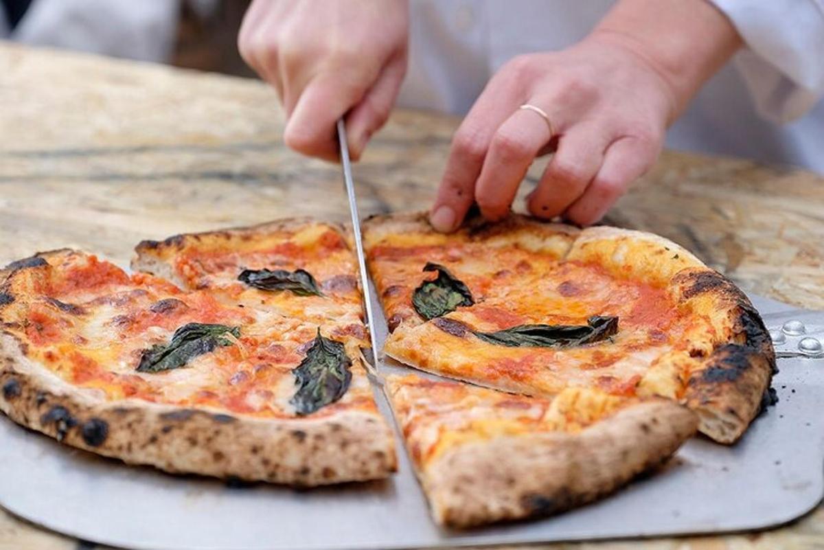 uma pessoa cortando uma pizza com garfo e faca