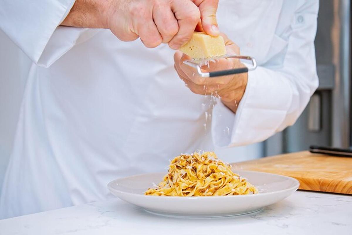 kokkur stráir osti á pastadisk