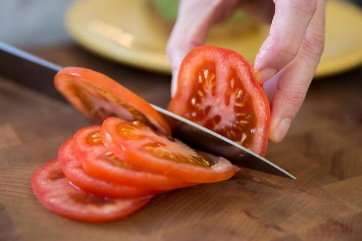 uma pessoa cortando um tomate com uma faca