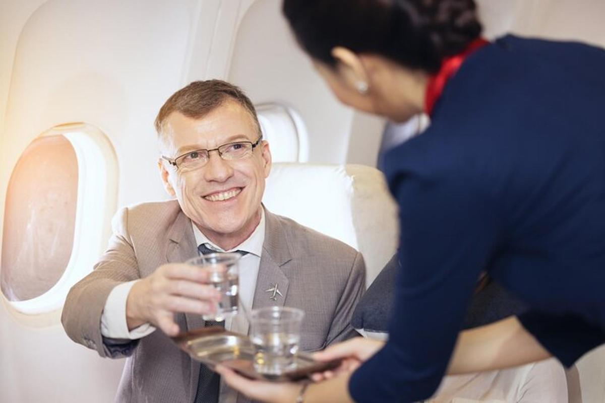 a man sitting on an airplane with a woman holding a glass