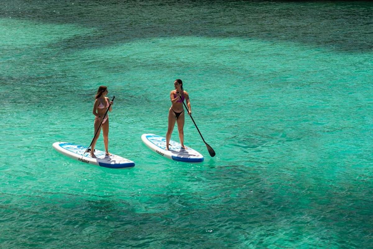 Două femei în costume de baie fac paddleboarding în apă