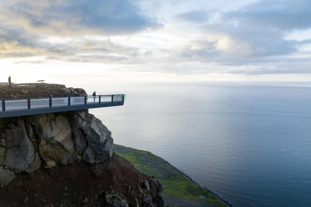 lidé stojící na mostě na útesu s výhledem na oceán