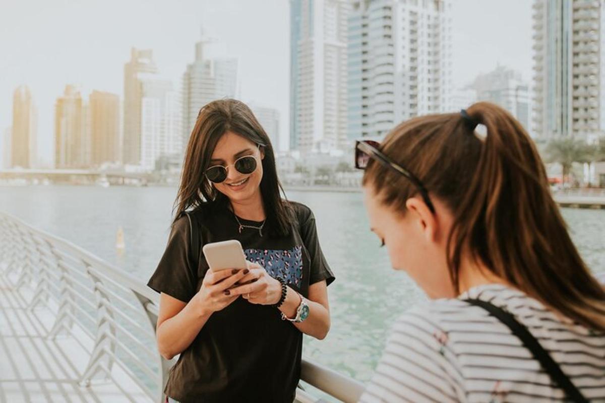 two women standing next to a river looking at a cell phone