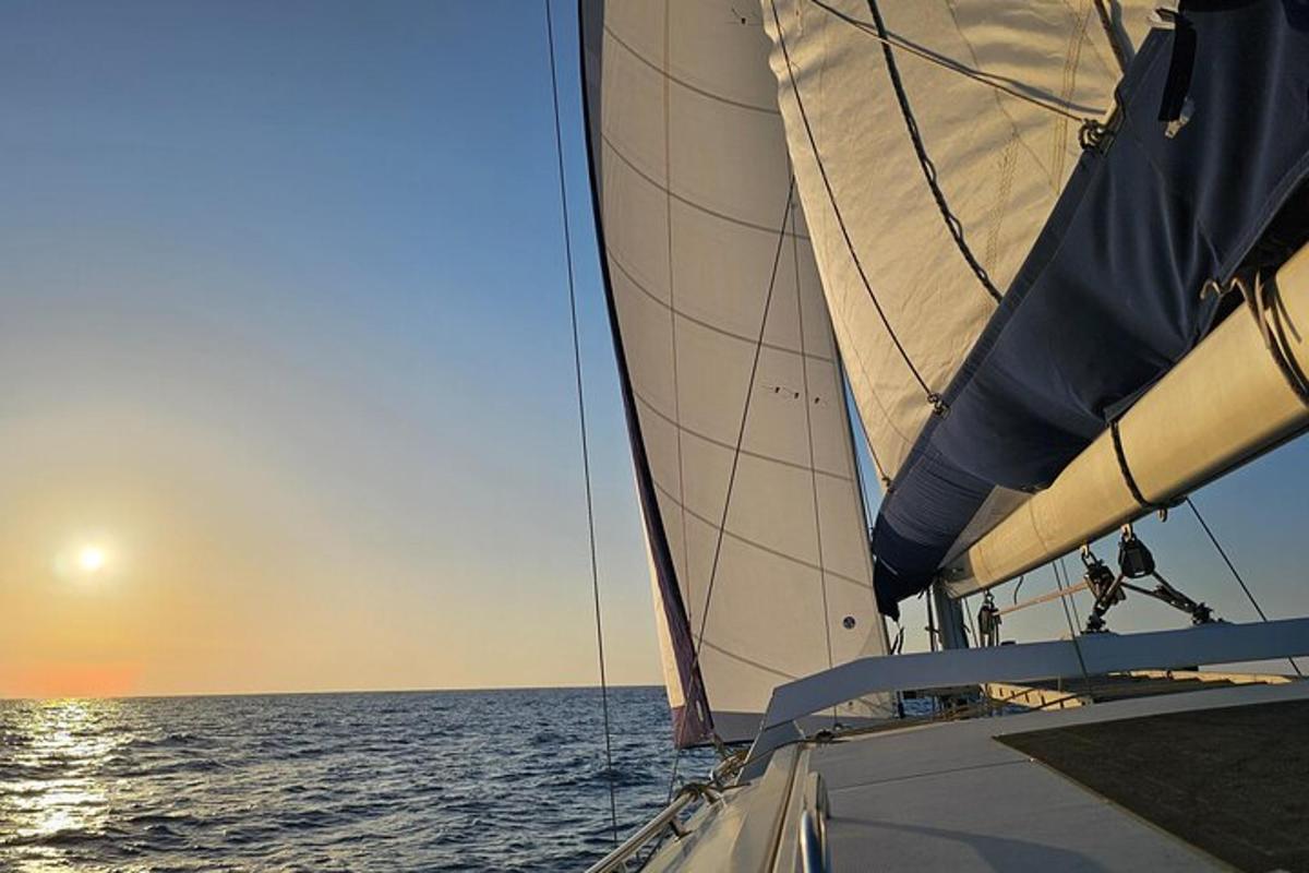 a sail boat in the ocean with the sun setting