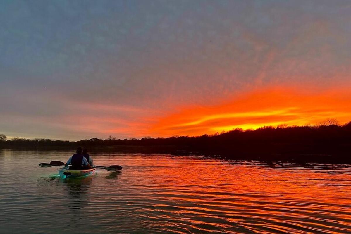 seseorang yang duduk di atas kayak di dalam air pada waktu matahari terbenam