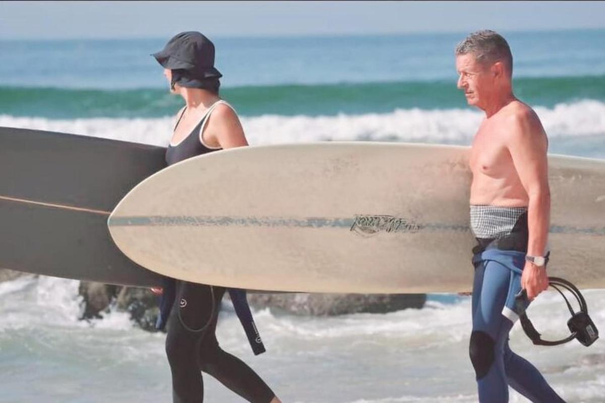 un uomo e una donna che camminano sulla spiaggia con una tavola da surf