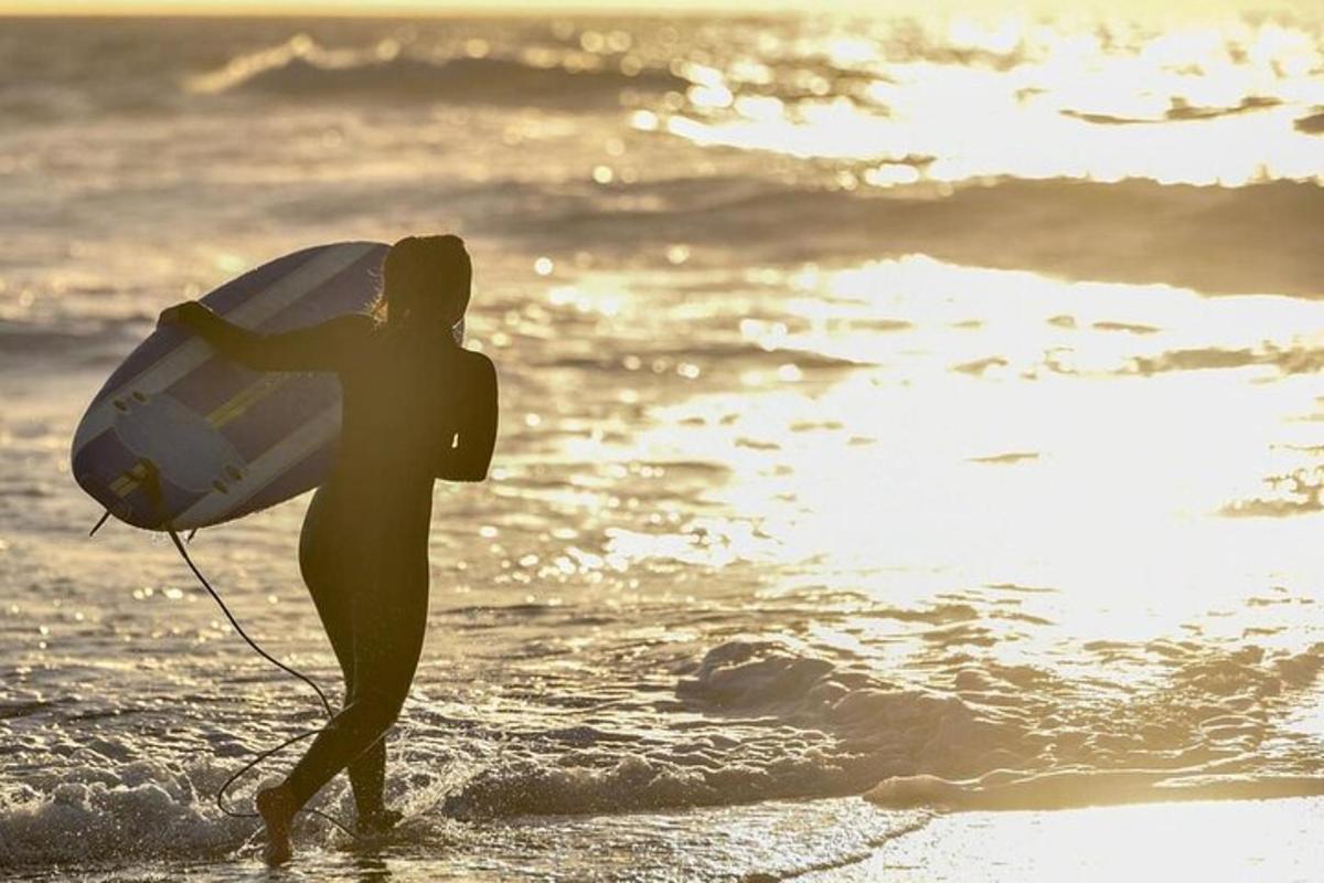 ženska, ki se sprehaja po plaži z desko za surfanje