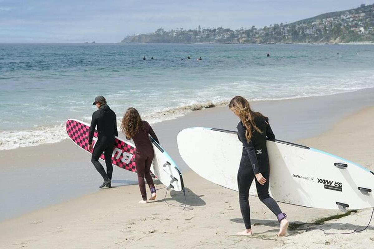 Tre surfere går på stranden med surfebrettene sine