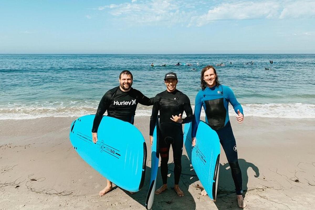 skupina treh ljudi, ki stojijo na plaži z deskami za surfanje
