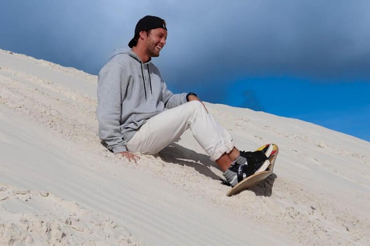 egy férfi ül egy homokdombon egy snowboarddal