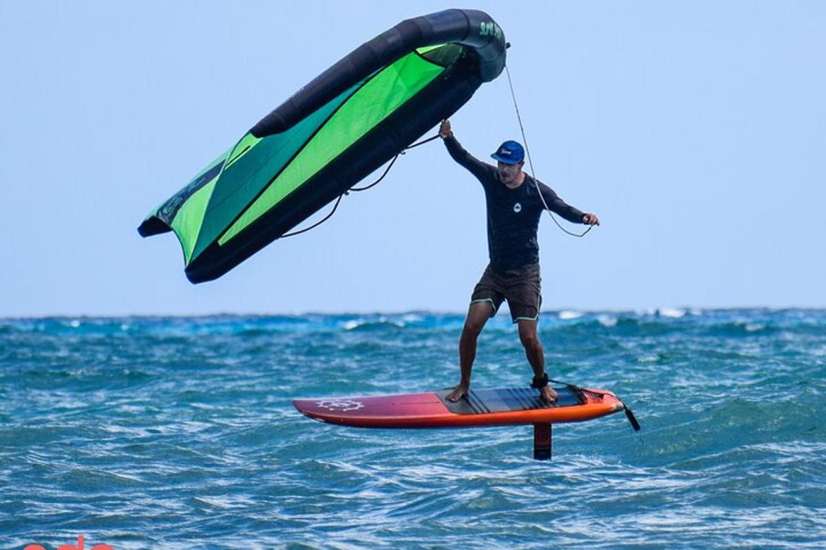 un home dret sobre una taula de surf sostenint un paracaigudes