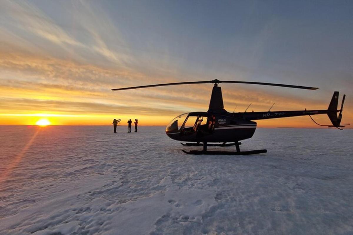 sebuah helikopter yang diletakkan di dalam salji dengan matahari terbenam