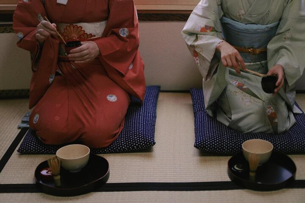 Dos personas sentadas en el suelo con tazas y palillos.