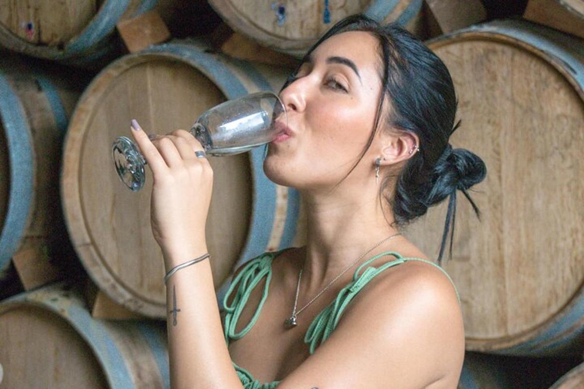 una donna che beve una bottiglia di vino davanti alle botti