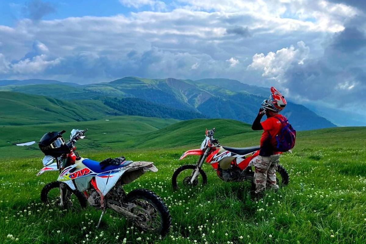 muž stojící vedle dvou terénních motorek na poli