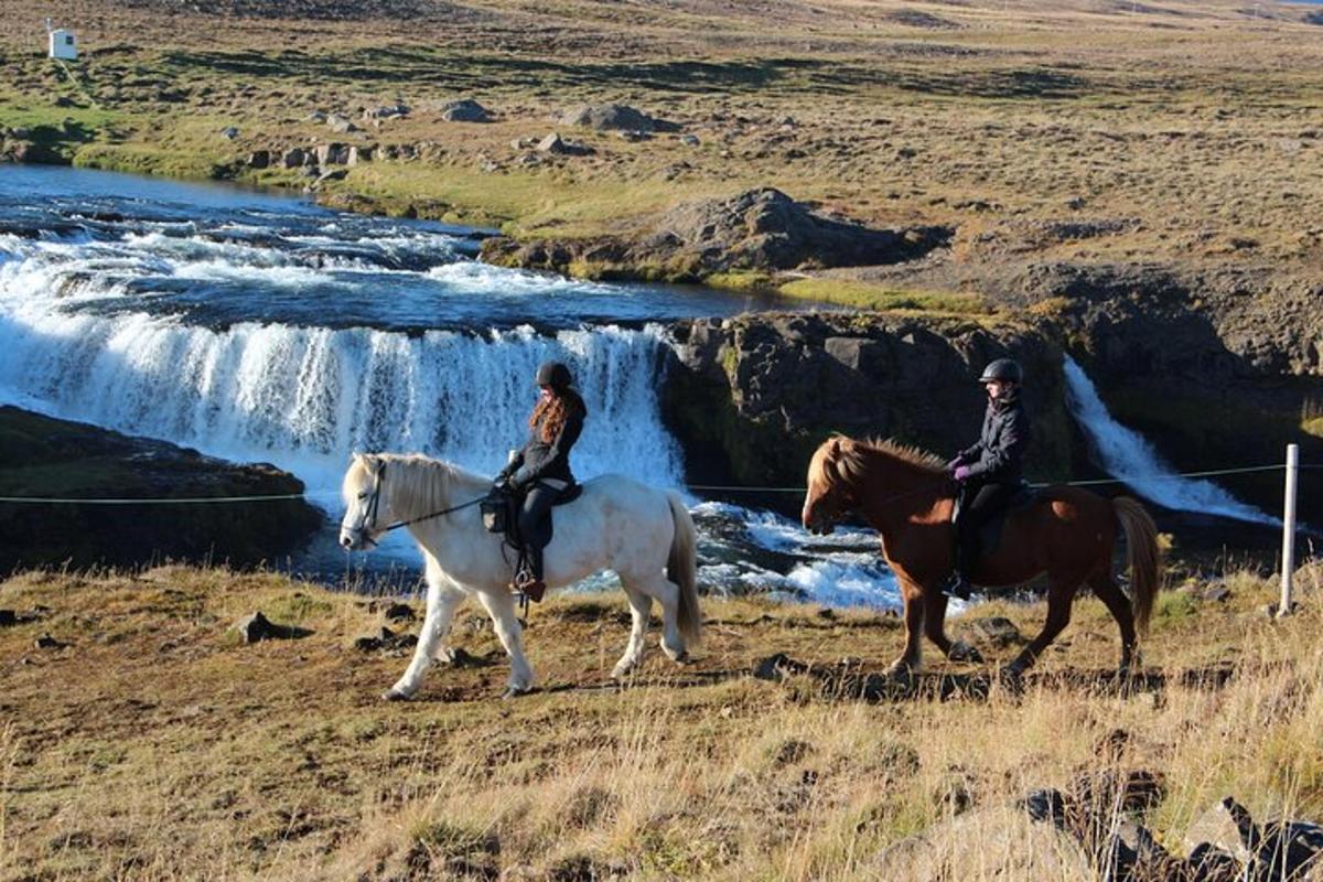 Dos personas montando a caballo frente a una cascada