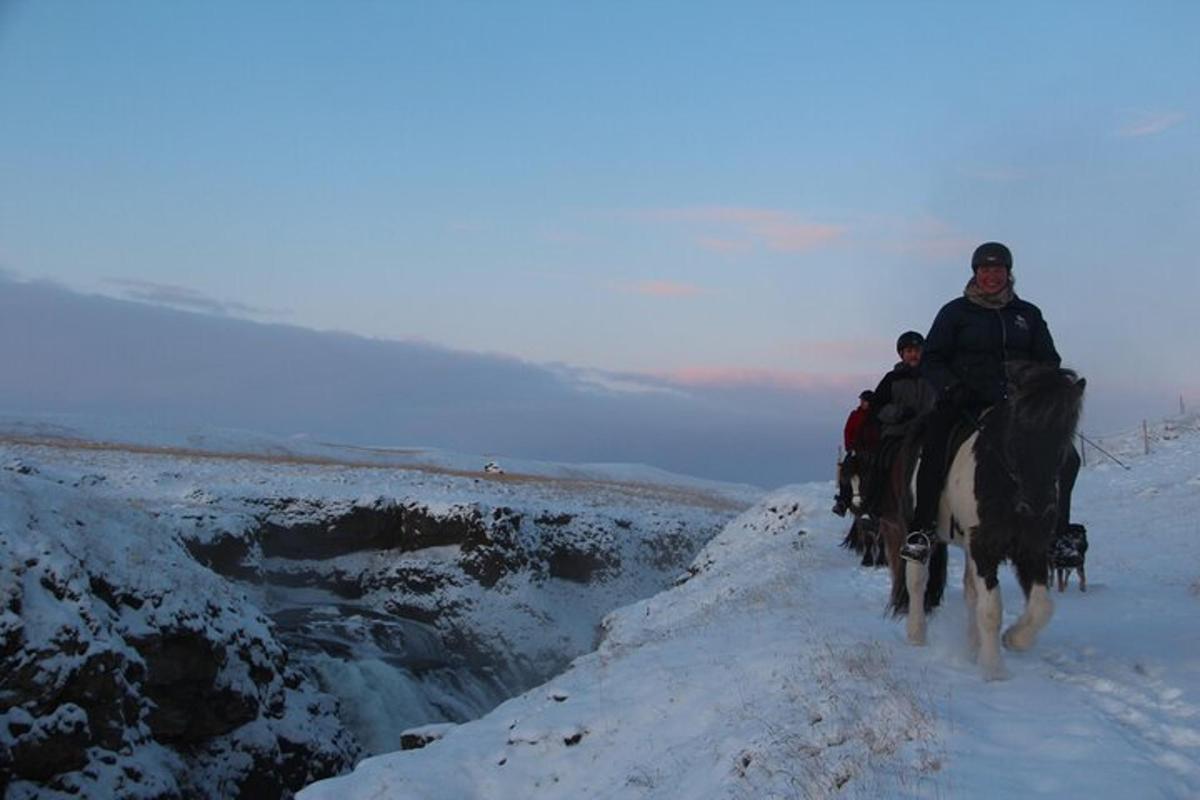 Dos personas montando a caballo por un sendero cubierto de nieve