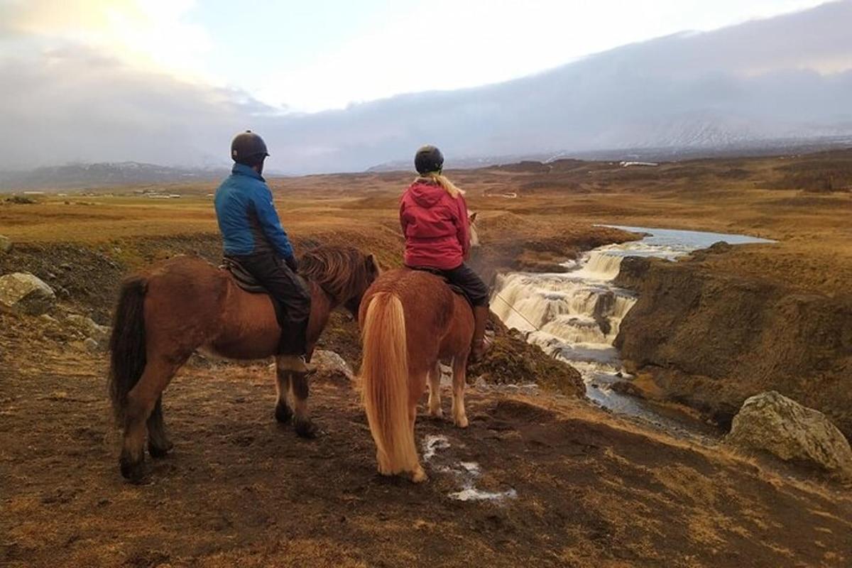 Dos personas montando a caballo en una colina cerca de un río